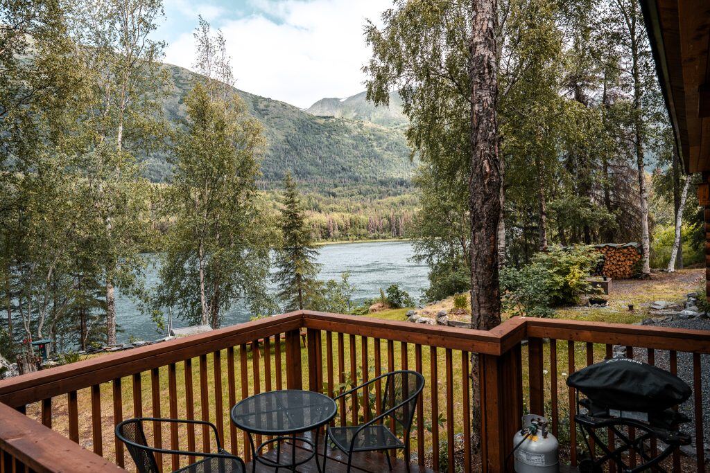 A wooden porch overlooking the bright blue Kenai River with forested hills in the background 